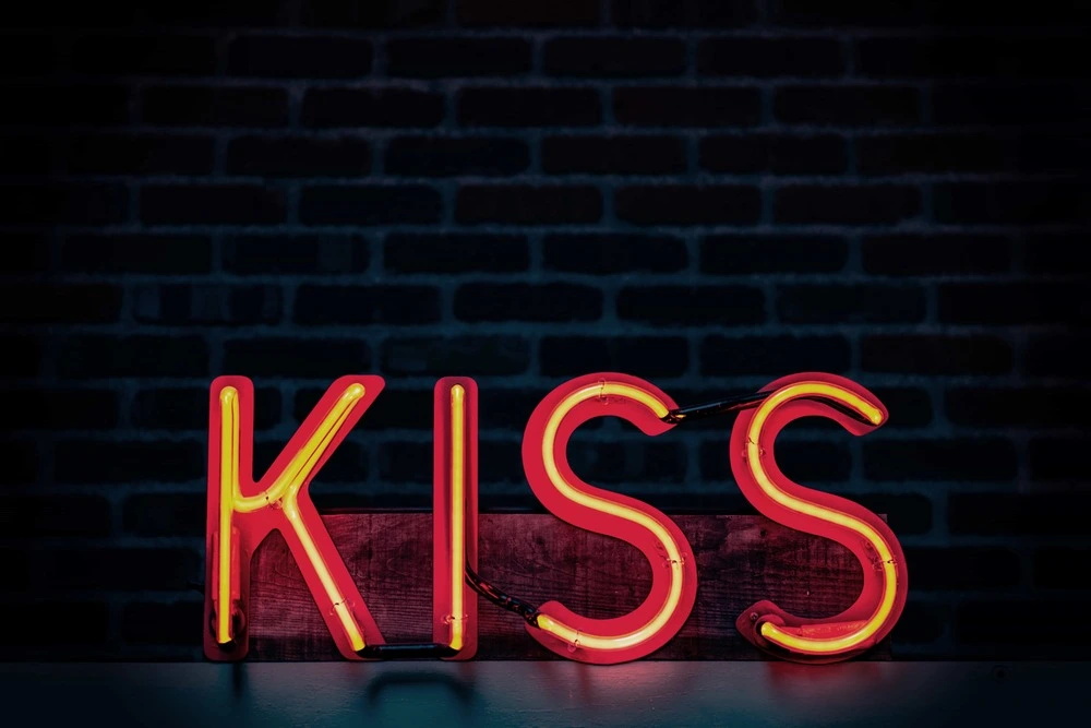 A glowing neon sign in the shape reading "KISS", symbolizing intimacy, passion, and the redefinition of sexual connection.
