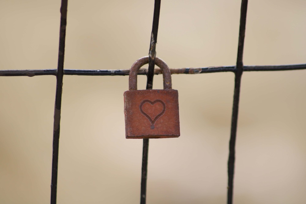A small heart-shaped lock attached to a fence, representing traditional views of commitment and contrasting the idea of love as growth and freedom rather than a restrictive “ball and chain.”