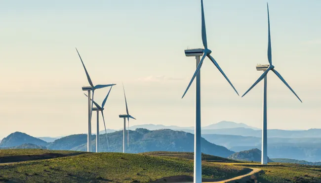 Landscape featuring wind turbines on rolling hills under a clear blue sky.