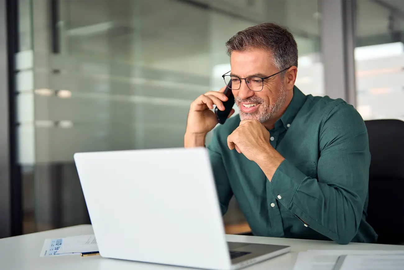 Man talking on his cell phone will looking at his laptop