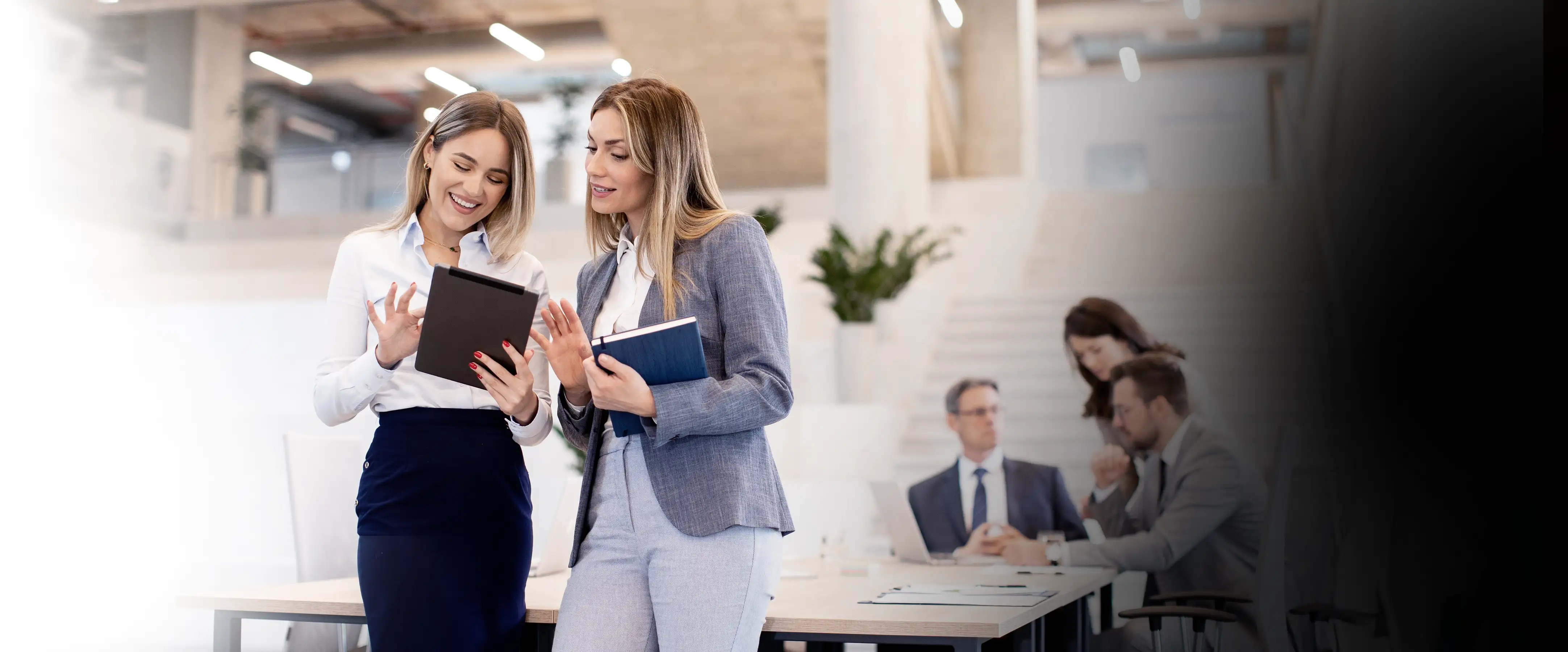 Two women standing together, smiling as the look at a tablet