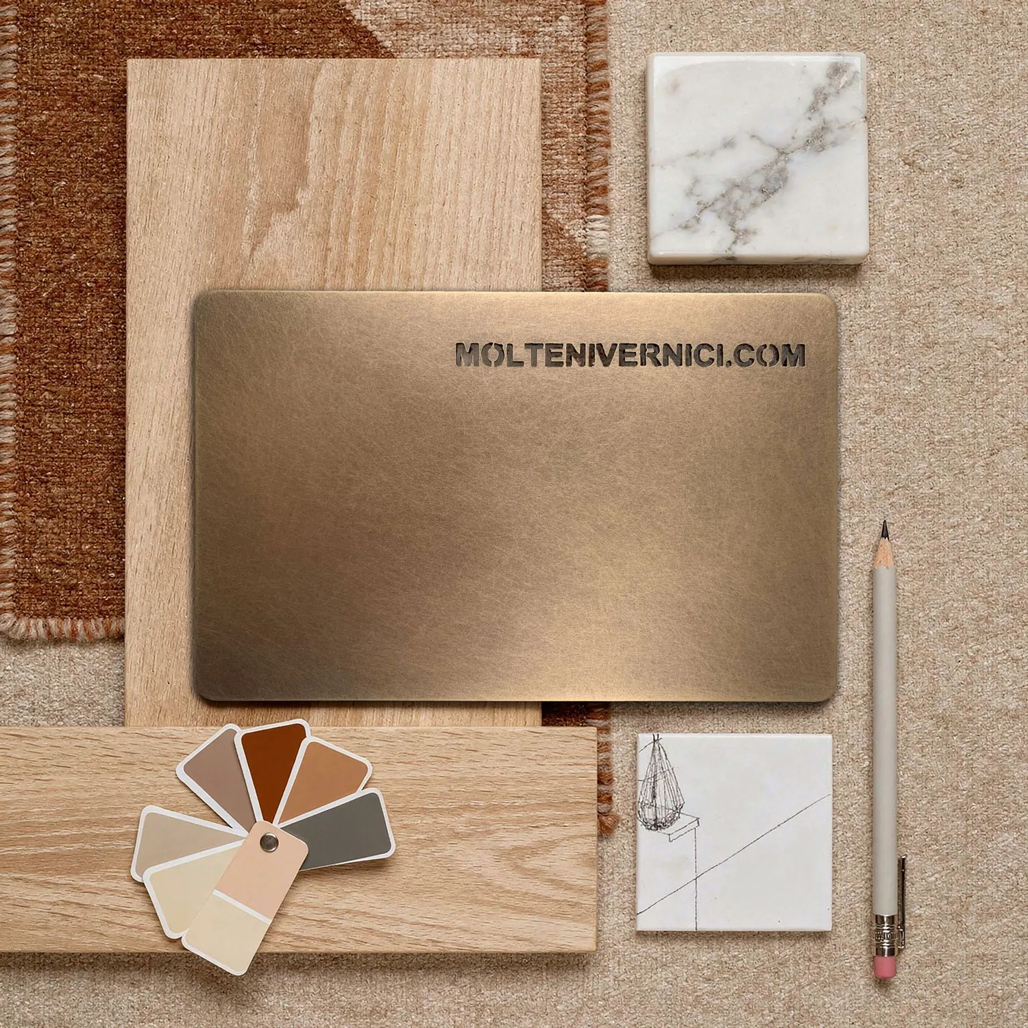 Campione rettangolare di finitura ottone bronzato su campioni di legno chiaro, piastrella di marmo bianco, palette di colori beige e marrone, matita grigia e piastrella bianca con disegno grafico.