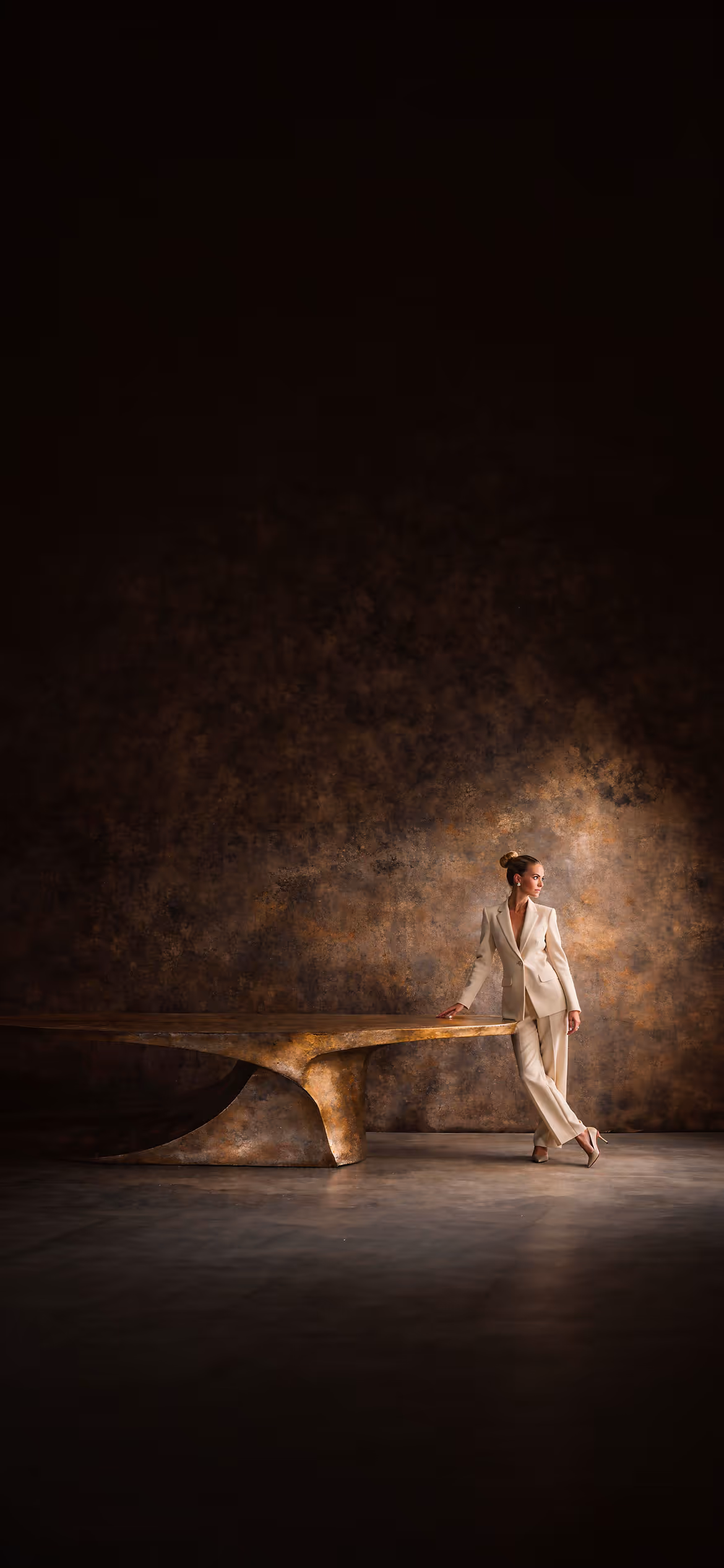 Sculptural hammered metal table with patinated surface and refined architectural setting, paired with an elegant female figure in a minimalist Maison aesthetic