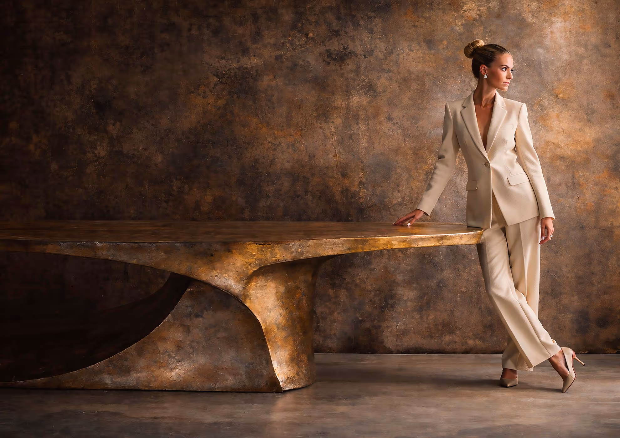 Sculptural hammered metal table with patinated surface and refined architectural setting, paired with an elegant female figure in a minimalist Maison aesthetic