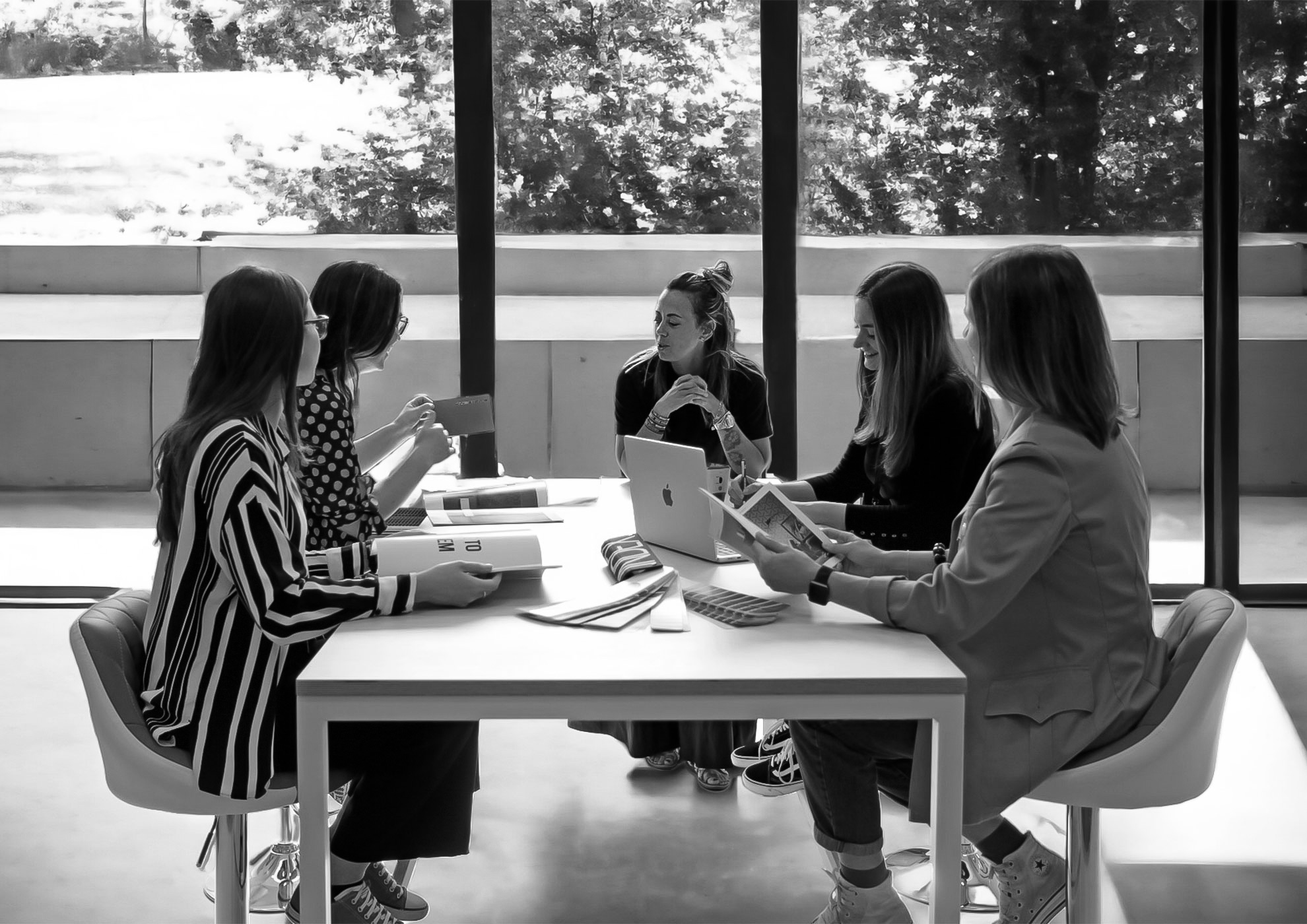 Cinq femmes réunies autour d'une table de travail près d'une fenêtre lumineuse