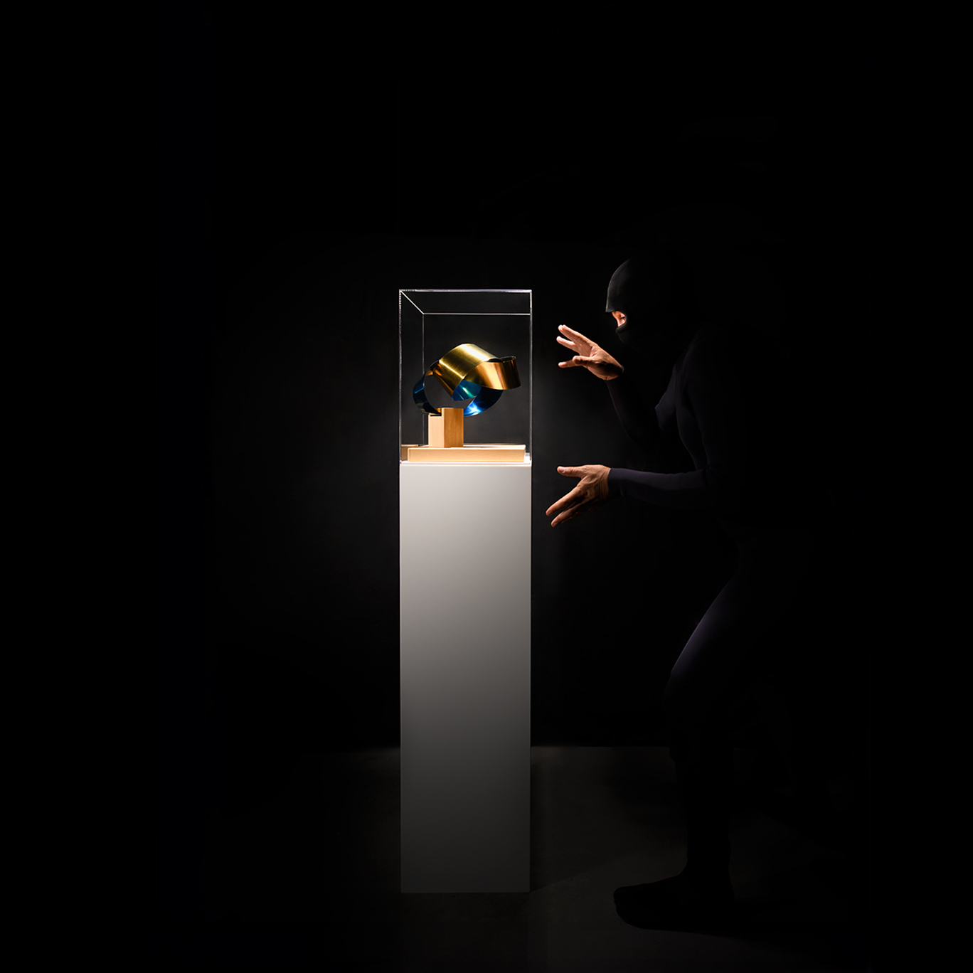 Black-clad figure gestures near golden object displayed in glass case