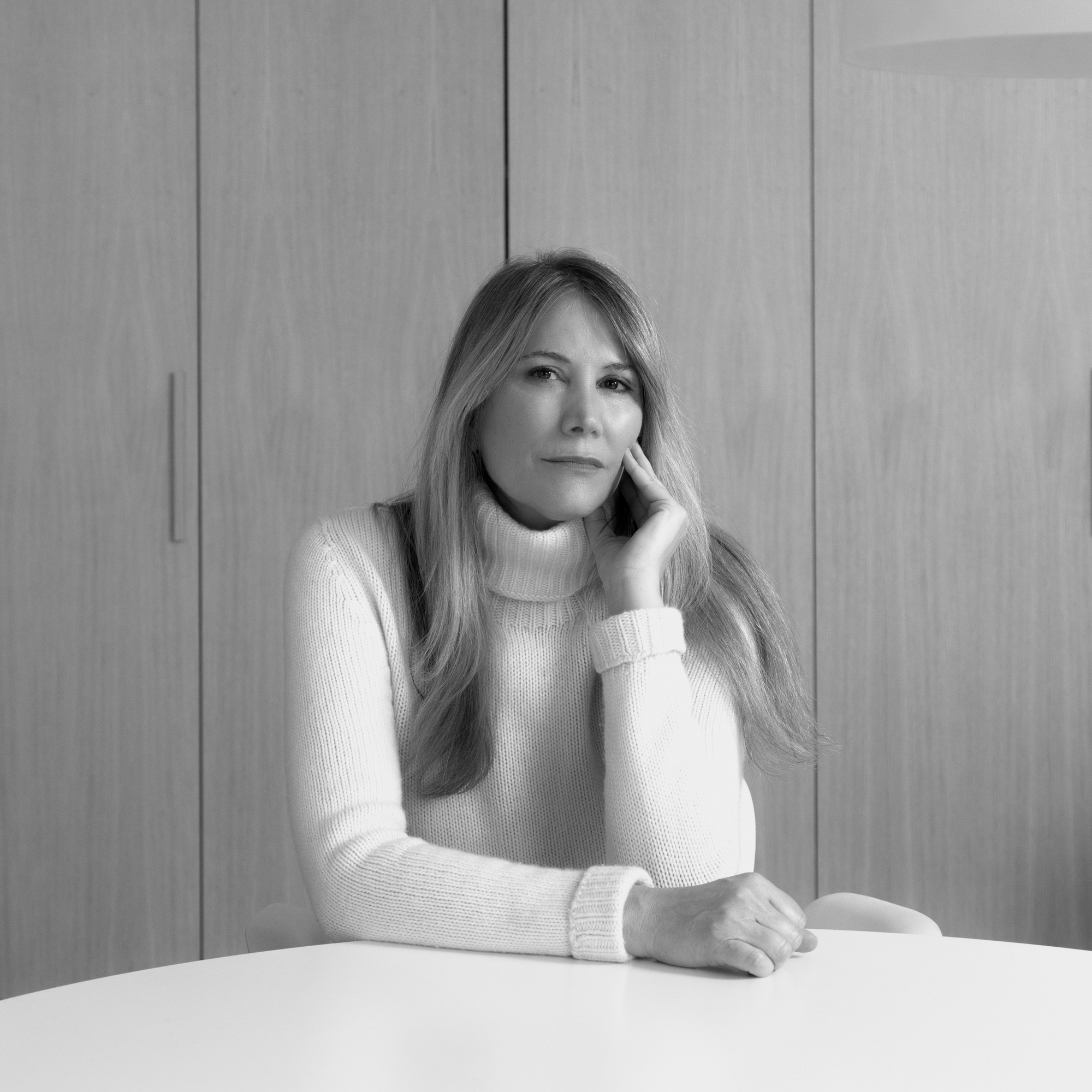 Woman in white turtleneck sweater leaning thoughtfully against wooden wall