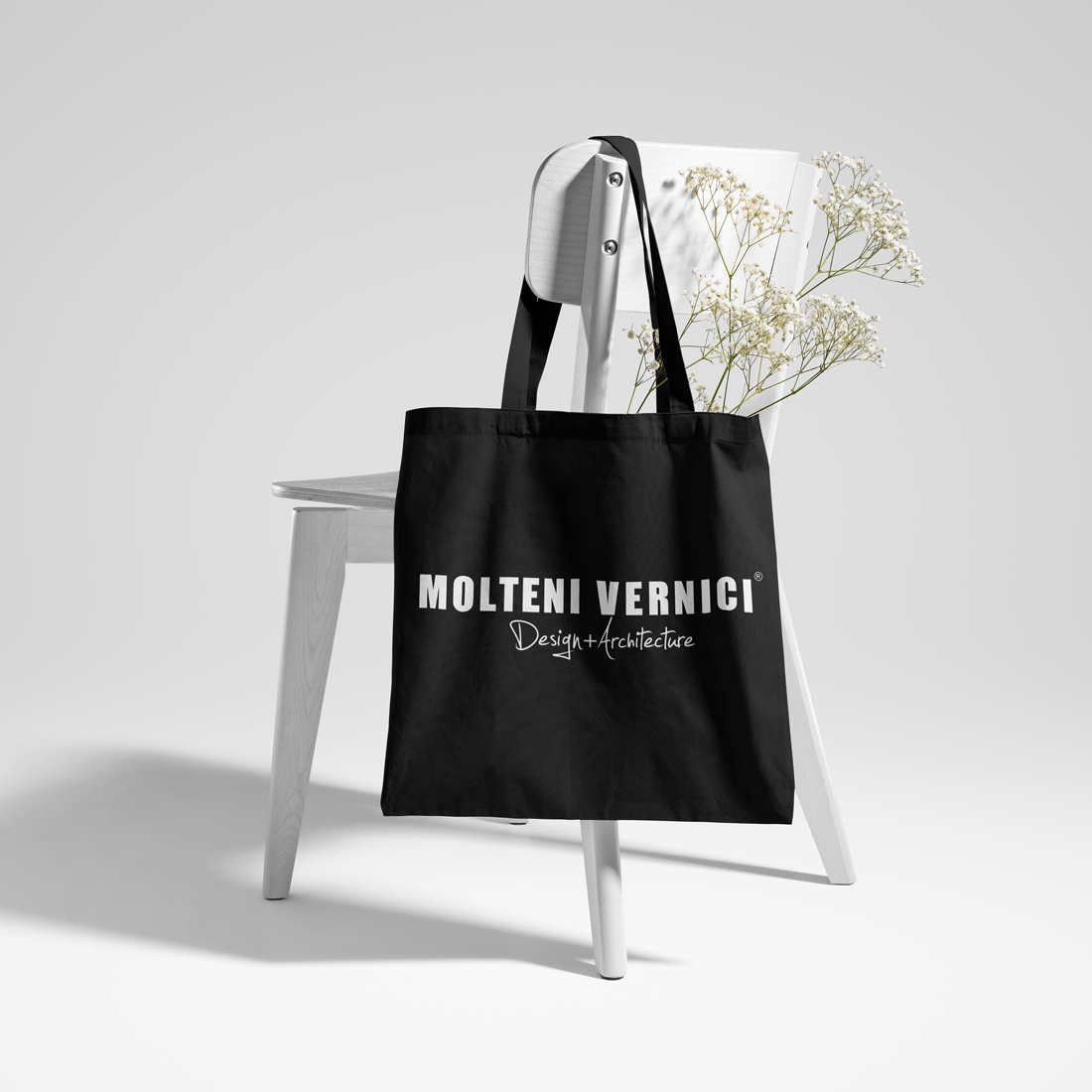 Sac noir Molteni Vernici avec des fleurs blanches sur une chaise blanche
