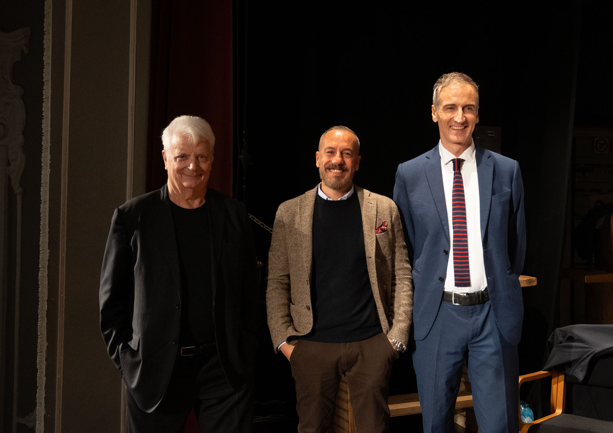 Trois hommes souriants en tenue élégante posant ensemble