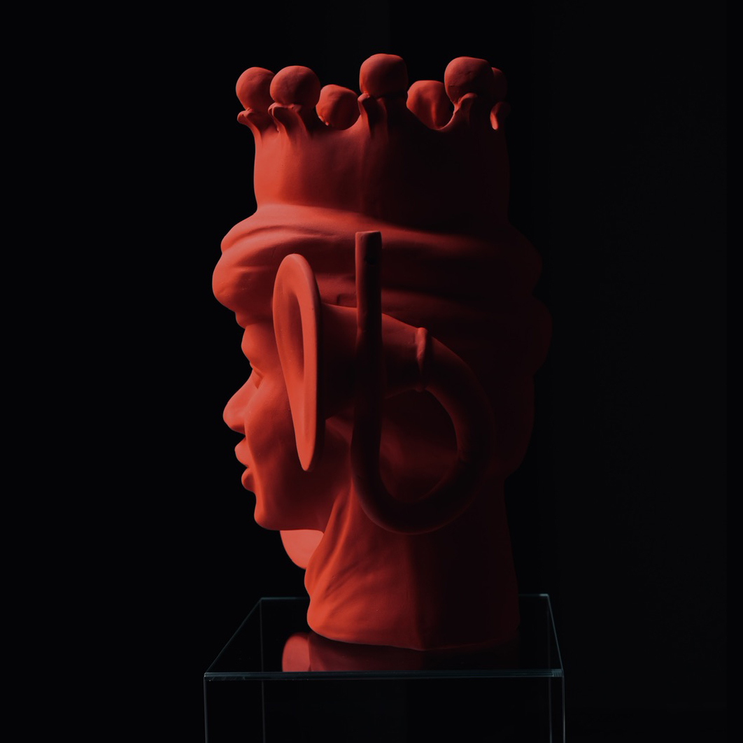 Sculpture rouge sombre d'un visage stylisé sur un socle noir