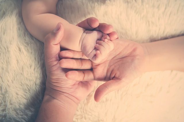Tiny baby feet resting gently in parent's hands on soft furry blanket