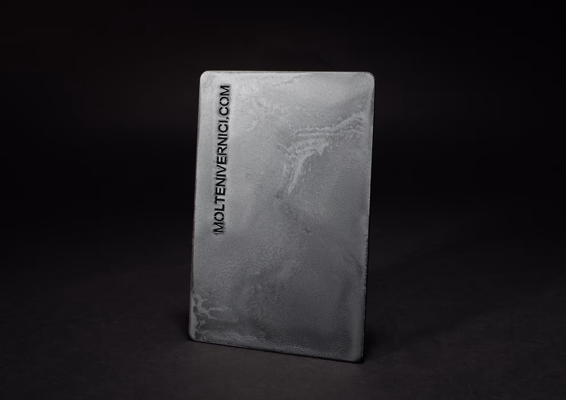 Muestra de acabados MOLTENI-VERNICI con textura metálica gris sobre fondo negro