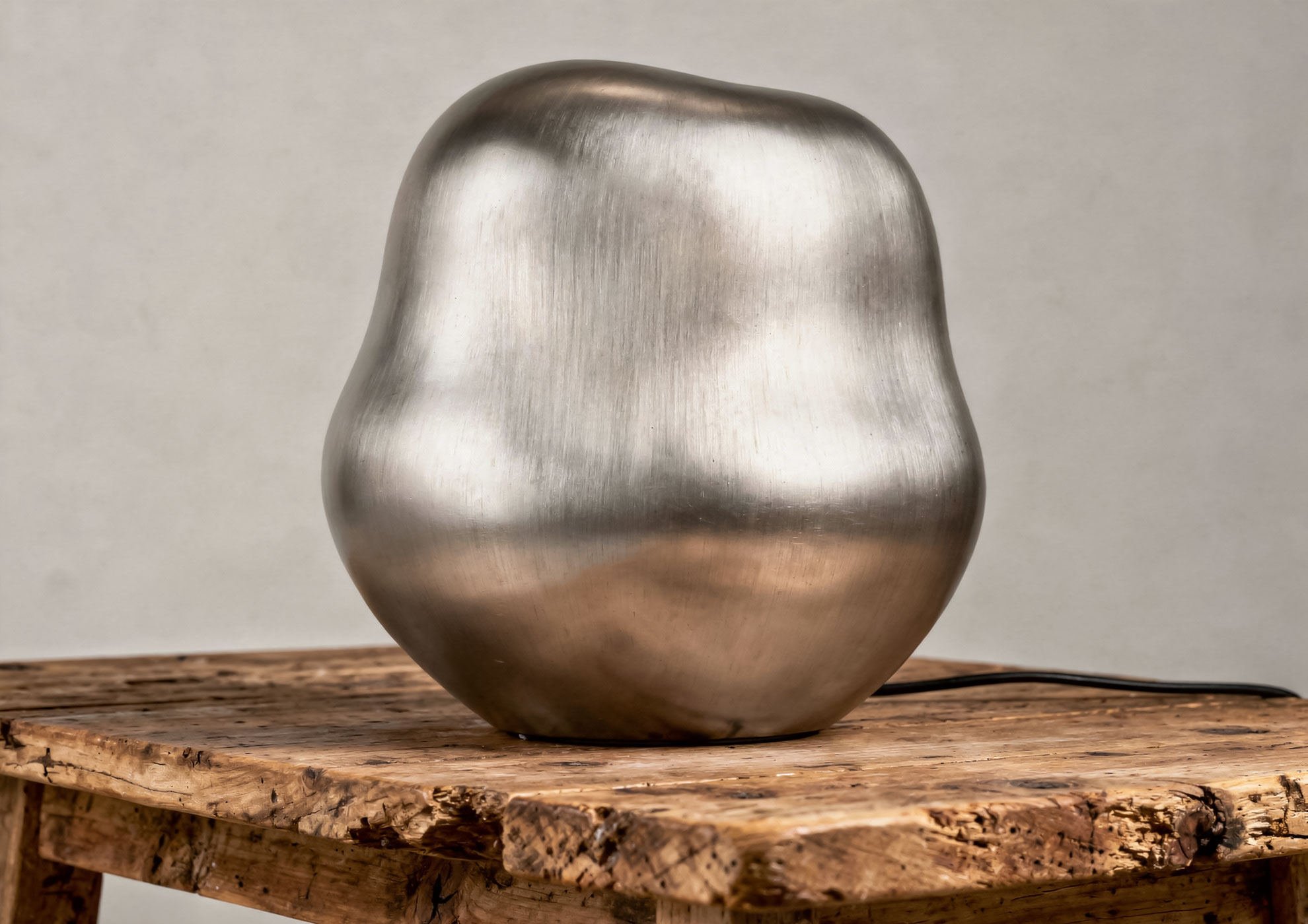 Designer table lamp with organic base coated in Never Brushed Spazzolato Argento Molteni Vernici finish, luxury metallic surface on natural wood support for contemporary interior.