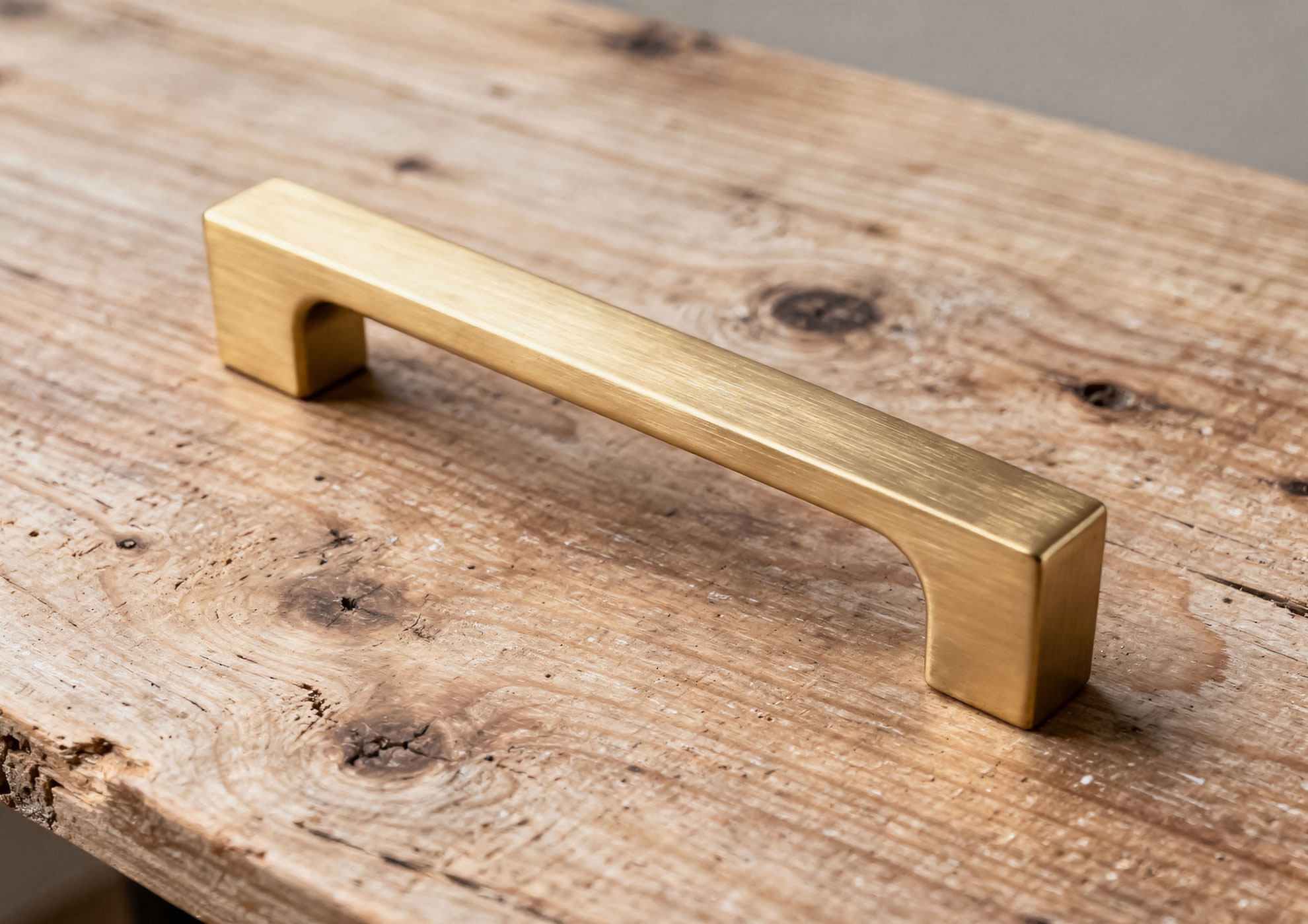 Minimalist handle in brushed gold metal with Never Brushed Molteni Vernici finish, design accessory applied to natural wood table, expression of contemporary elegance and Italian craftsmanship.