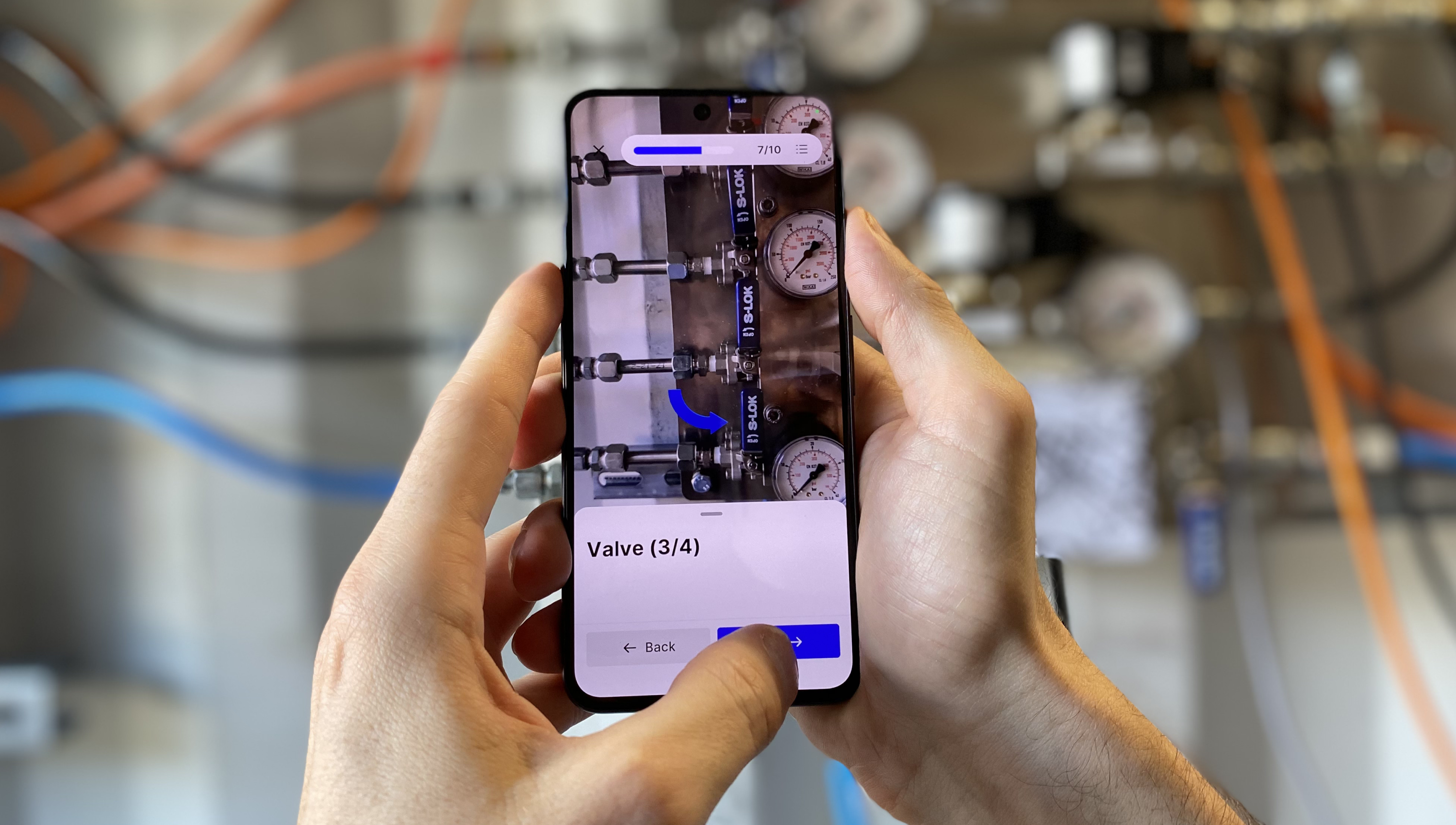 Technician holding a smartphone displaying augmented reality guidance for operating a valve board from P-Wave manufacturer.