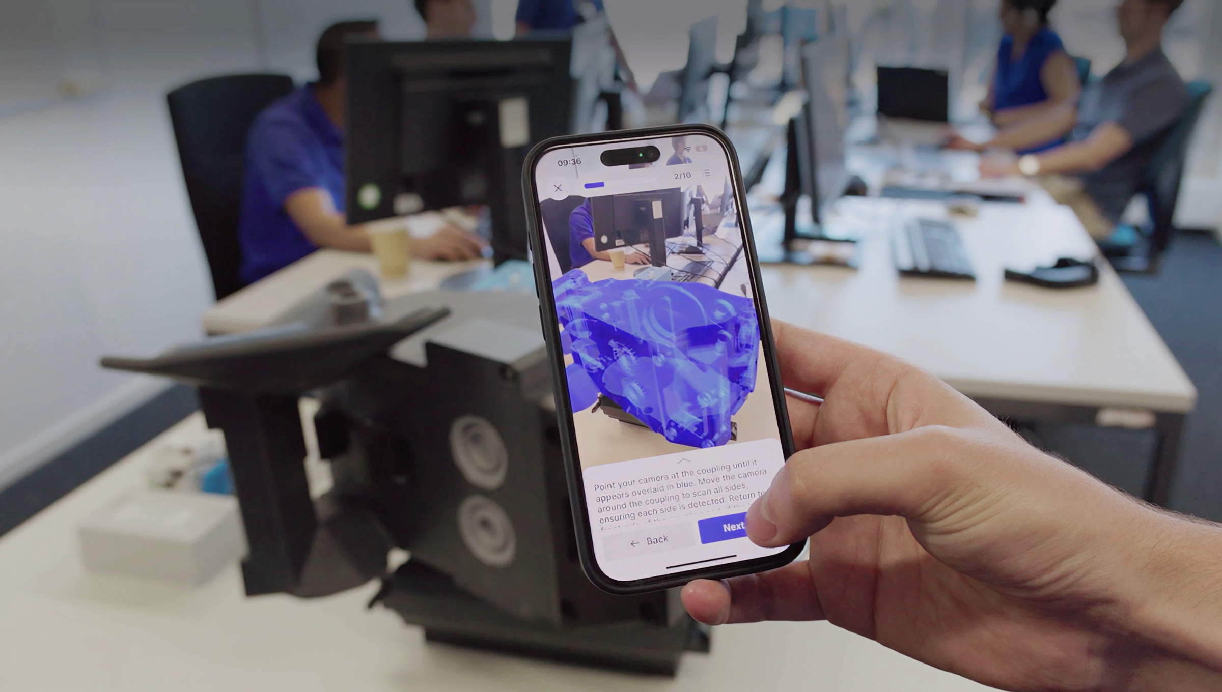 Person using a smartphone to view an augmented reality overlay on a train clutch prototype.