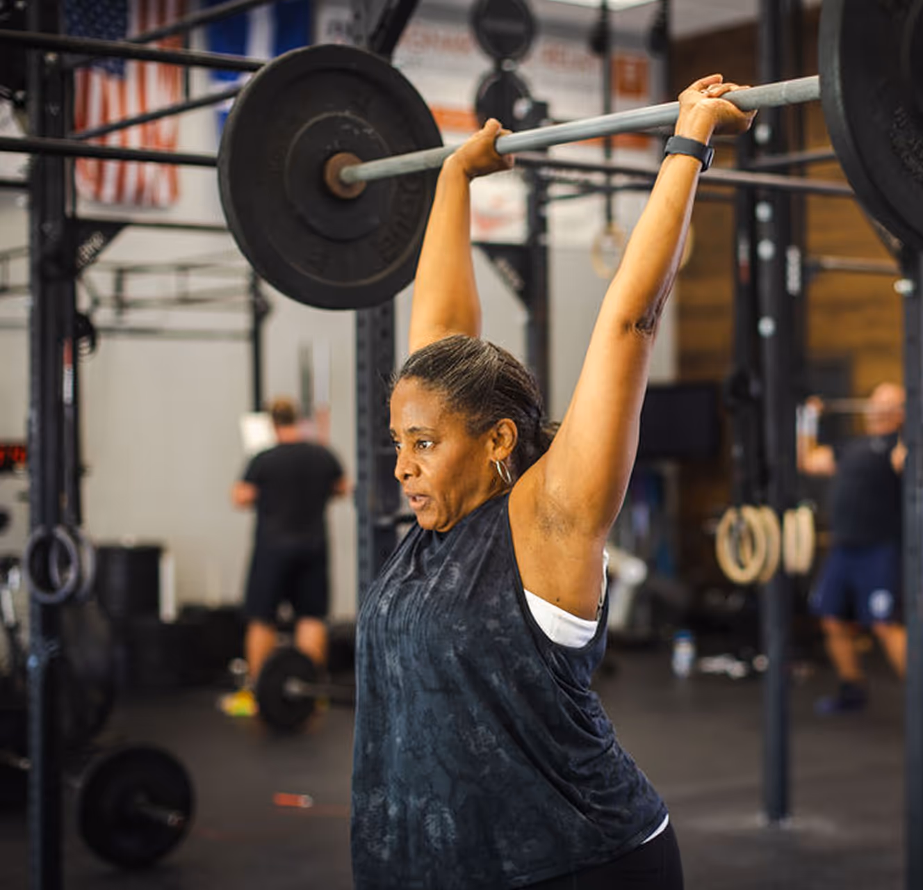 Woman lifting a barbell overhead in a gym during a workout.