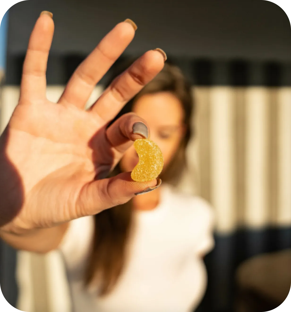 Close-up of a hand holding a MegaFood gummy vitamin with a woman blurred in the background.
