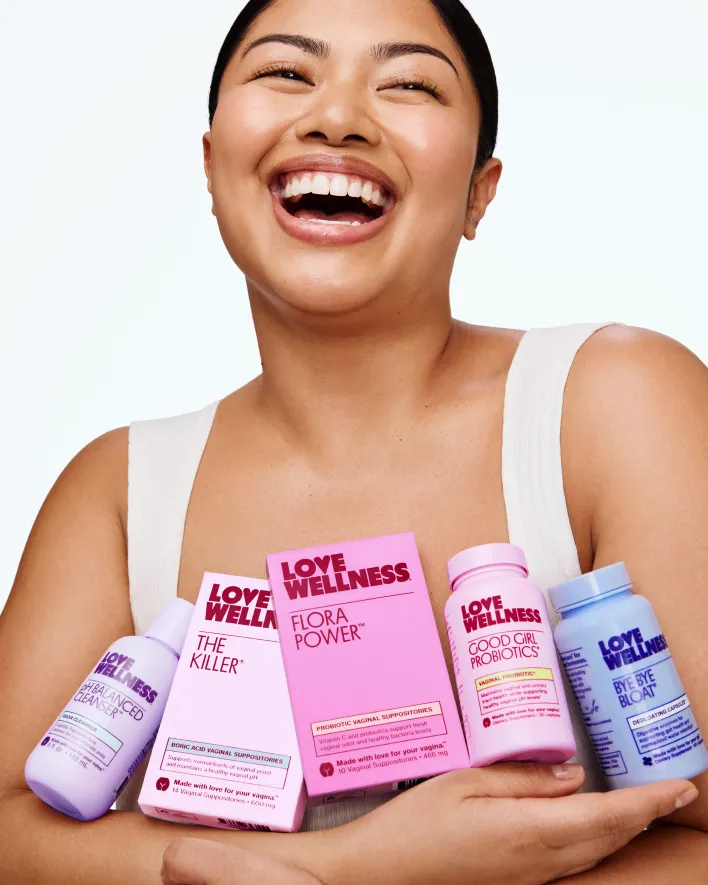 Woman laughing while holding an assortment of Love Wellness feminine care products.