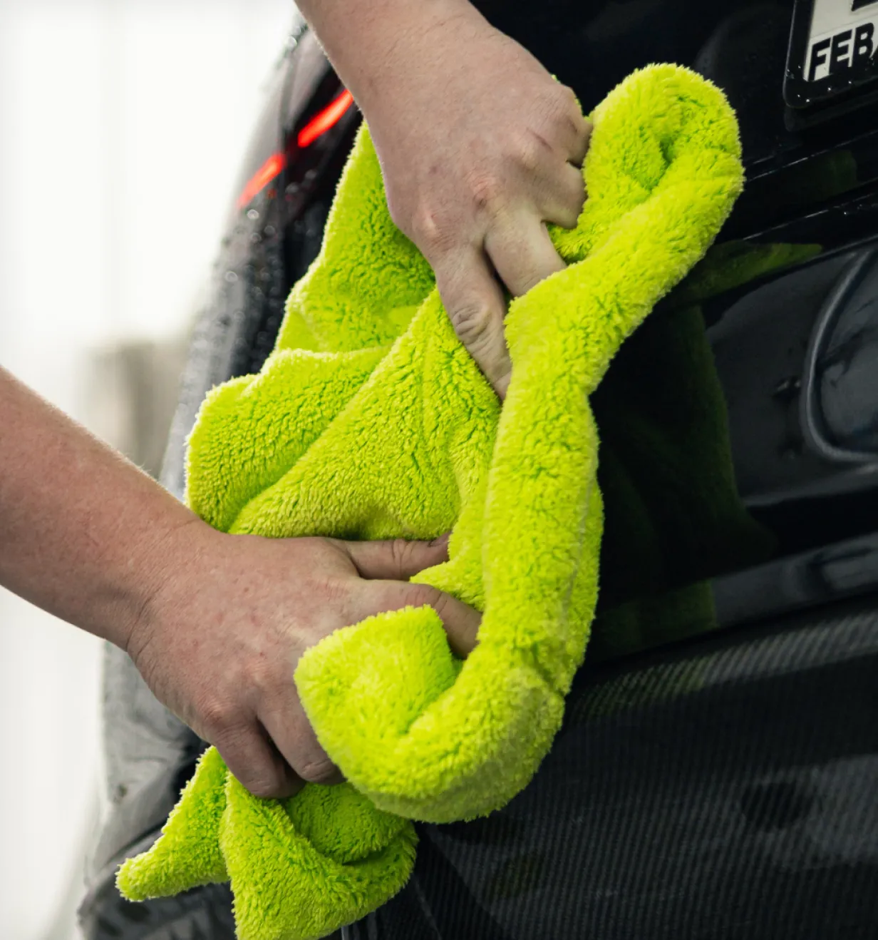 Hands wiping a black car's paint with a bright green Autofiber microfiber towel.