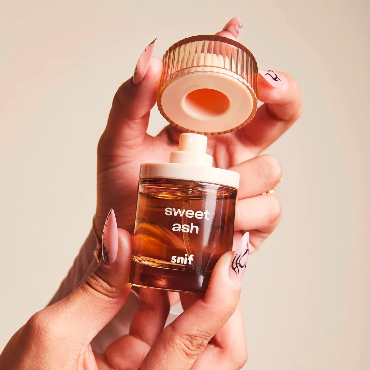 Hands holding an open bottle of Snif 'Sweet Ash' fragrance.