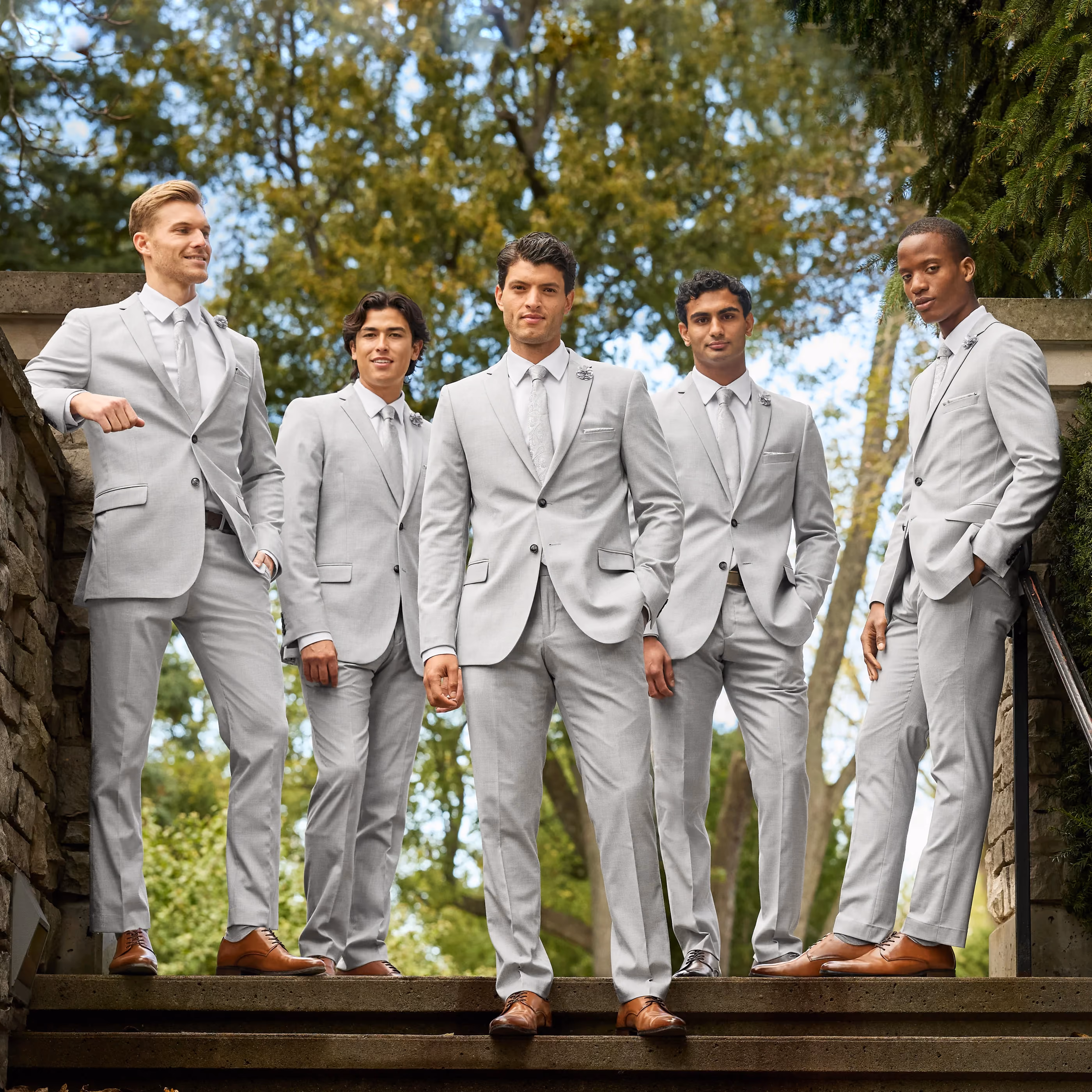Five groomsmen in matching light gray Tip.Top suits standing on outdoor stone steps.