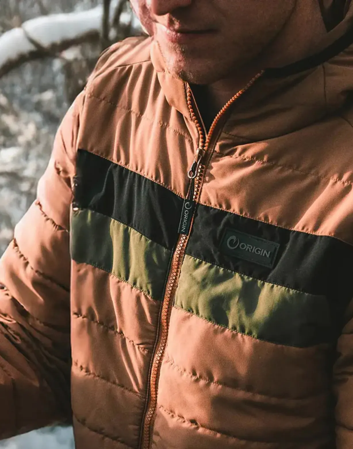Close-up of a man wearing an Origin brand quilted puffer jacket in rust, black, and olive.