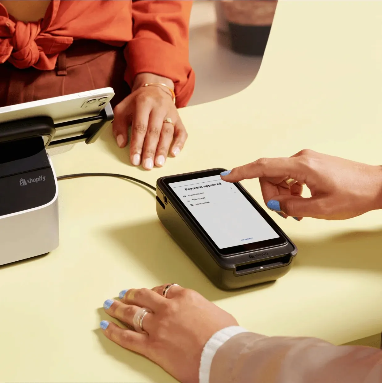 Close-up of a Shopify POS terminal displaying a payment approved screen as a customer taps to pay.