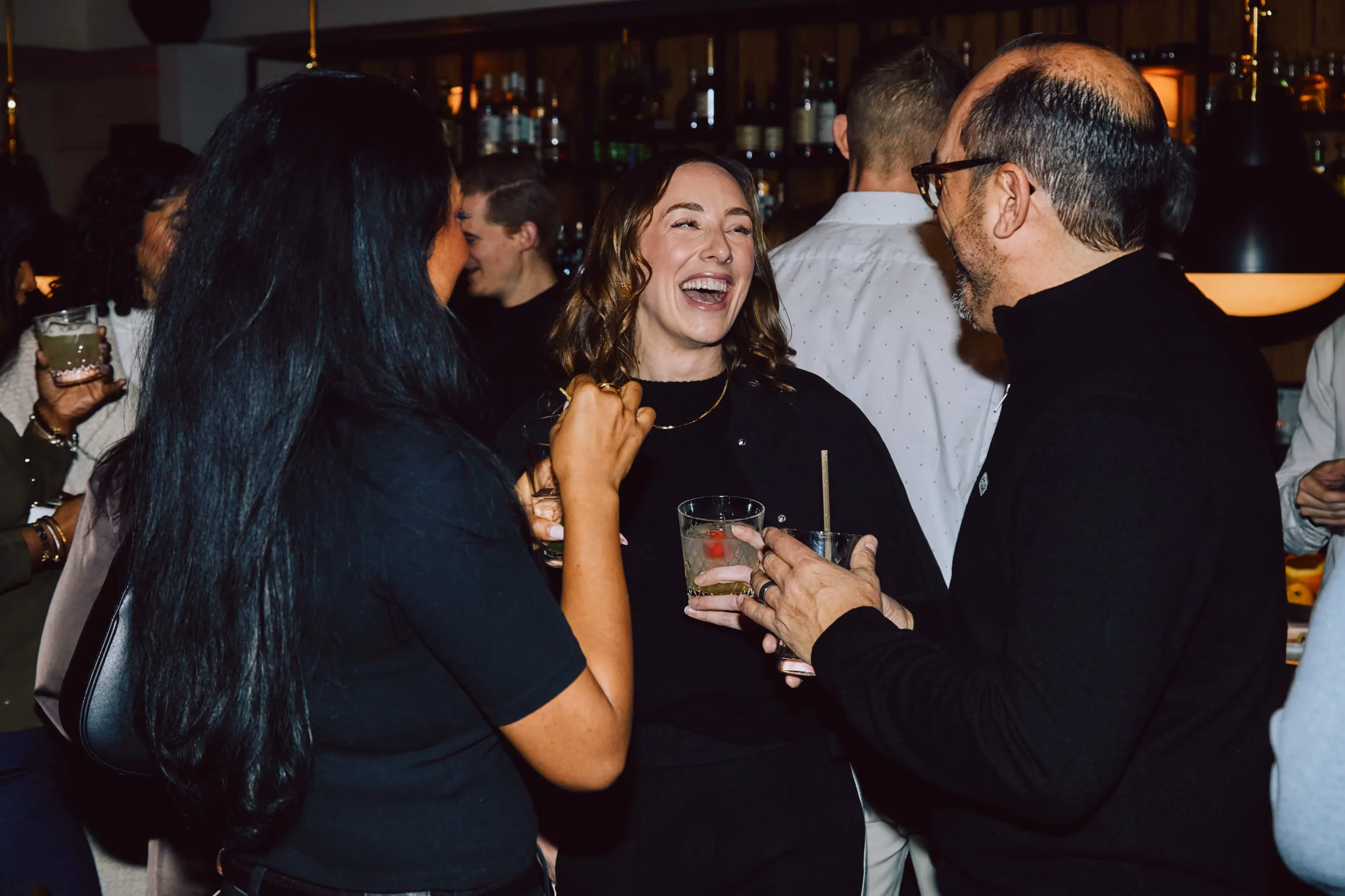 Three attendees laughing together while holding drinks at an ehouse networking event.