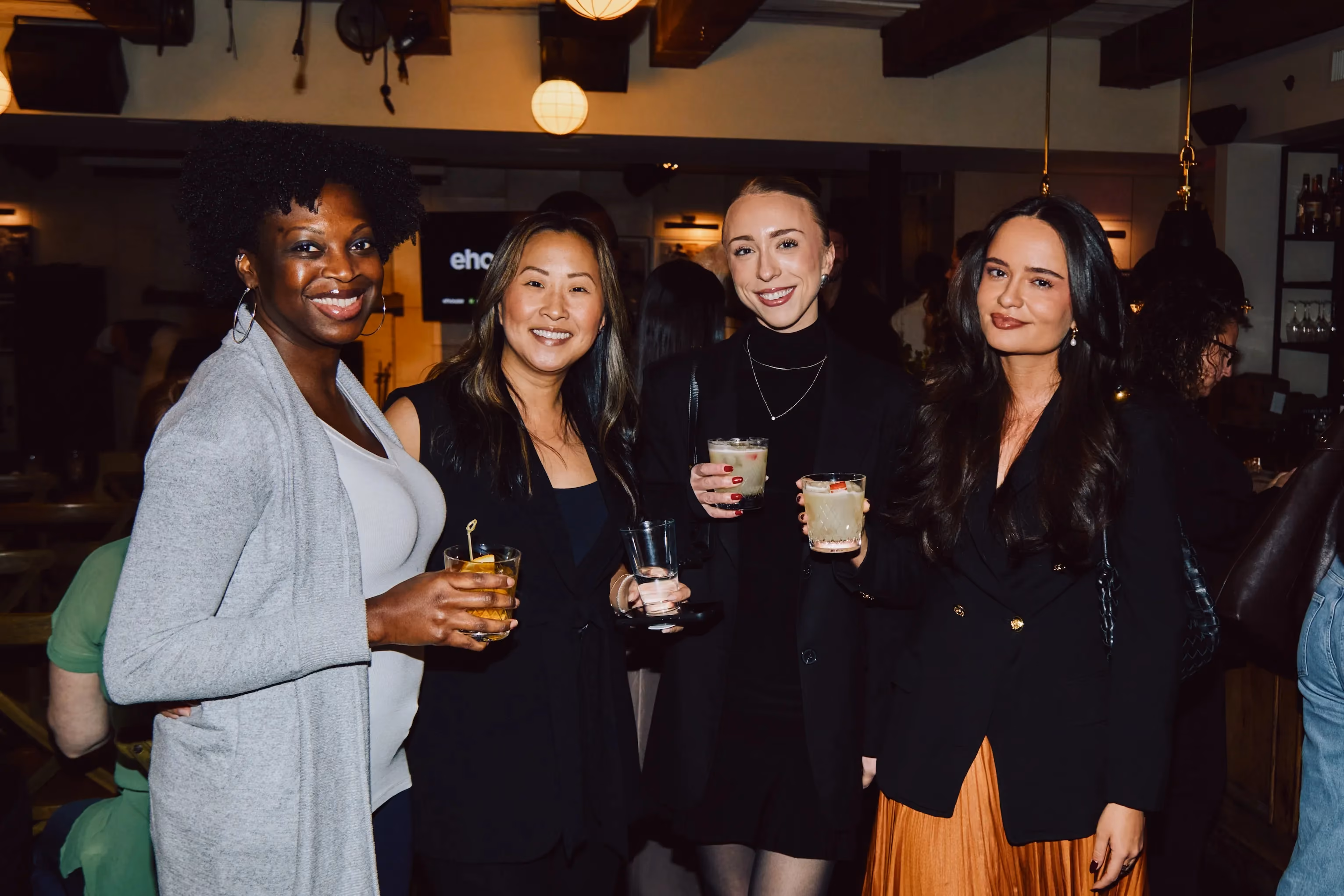 Four women smiling with cocktails at an ehouse networking event.