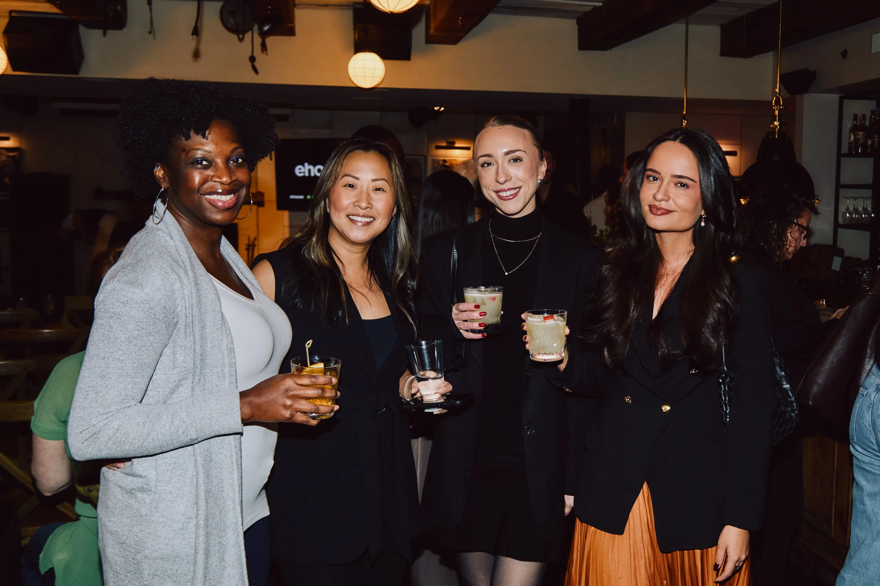 Four women smiling with cocktails at an ehouse networking event.