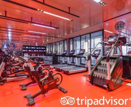 Salle de sport luxueuse de l'Hôtel Lutetia Paris avec vélos elliptique et tapis de course dans un décor lumineux et rouge