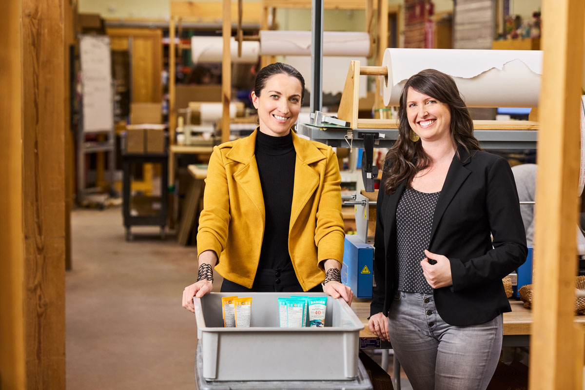 The heads of Badger Balm stand in their warehouse in front of a storage bin of product