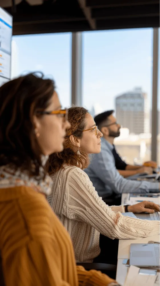 A woman wearing glasses and a yellow shirt is working on a computer.