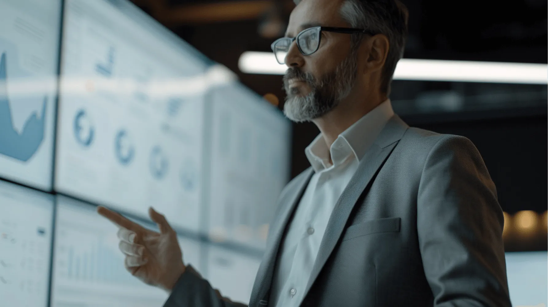 A man in a suit and glasses is pointing at a computer screen.