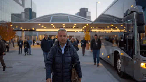 A man in a blue coat and brown bag walking in front of a bus.