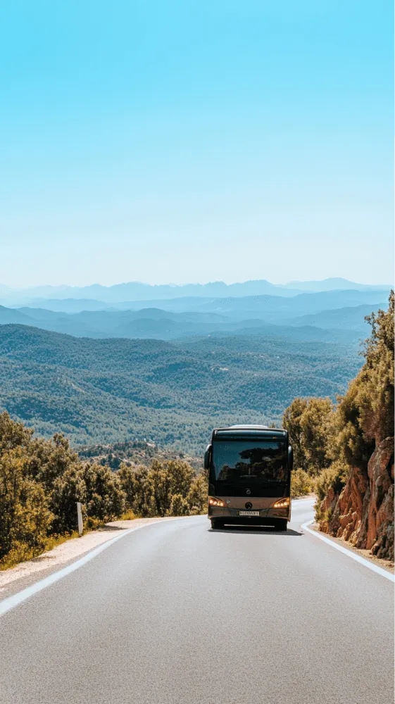 A bus is driving down a road with mountains in the background.
