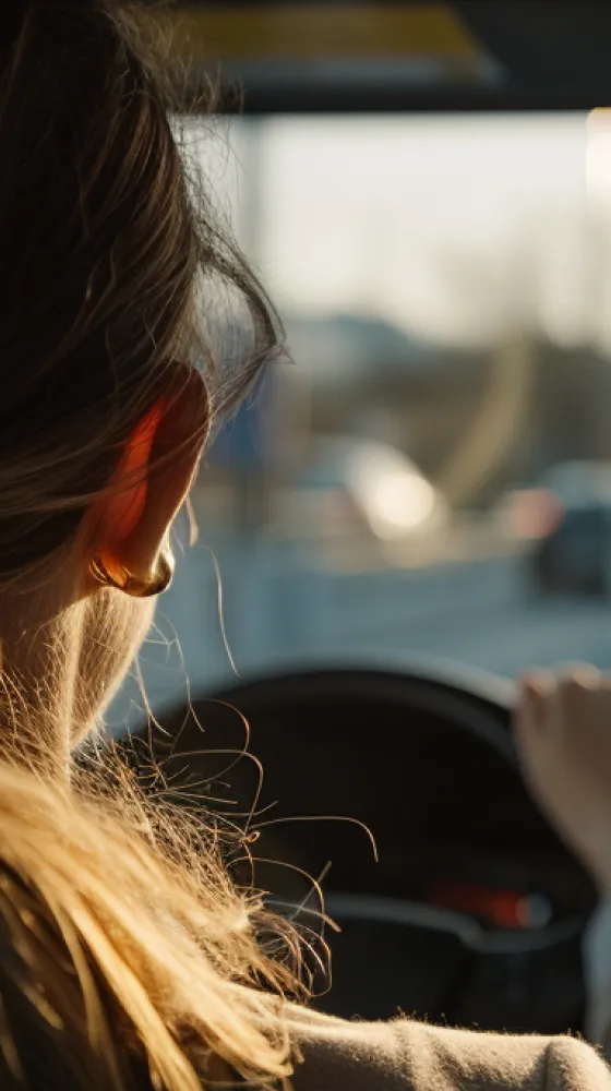 A woman with blonde hair and earrings is driving a car.