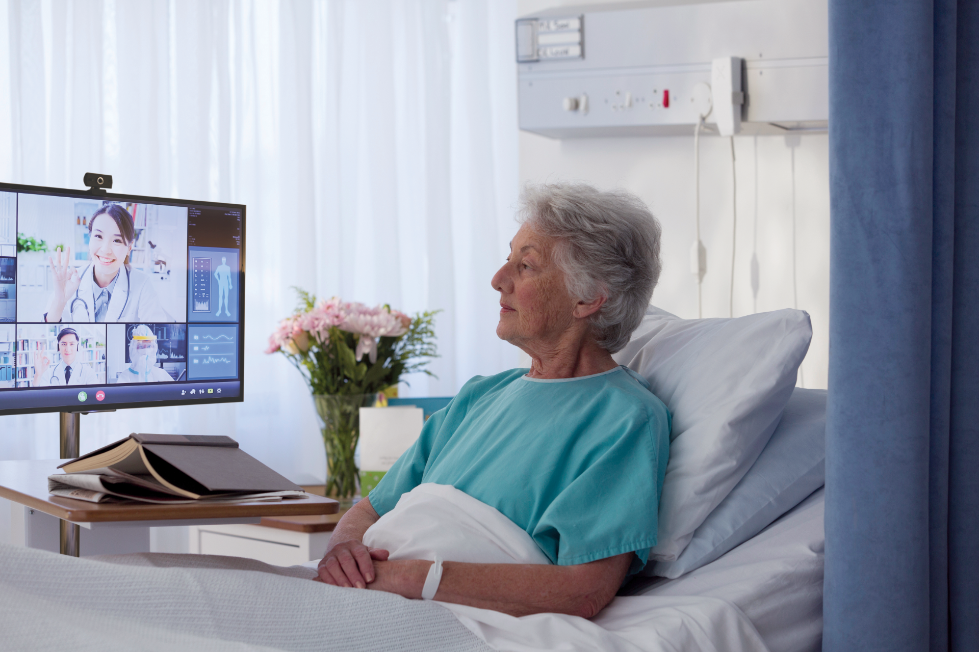 Elderly woman patient in a hospital bed talking to doctors via telehealth conference