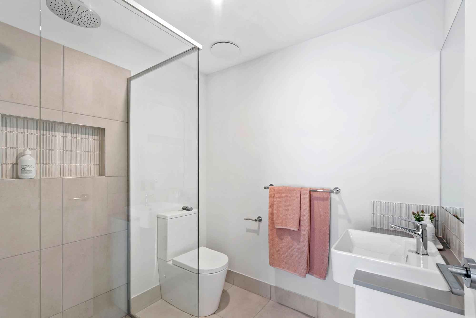 Modern bathroom with walk-in glass shower, rainfall showerhead, built-in tiled niche, floating vanity, chrome fixtures and soft neutral tiles in a contemporary new build.