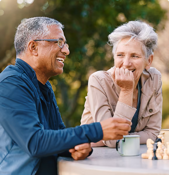 Couple laughing together over coffee and chess, representing Northeast Wealth's Creating Freedom financial strategy for people in their 50s
