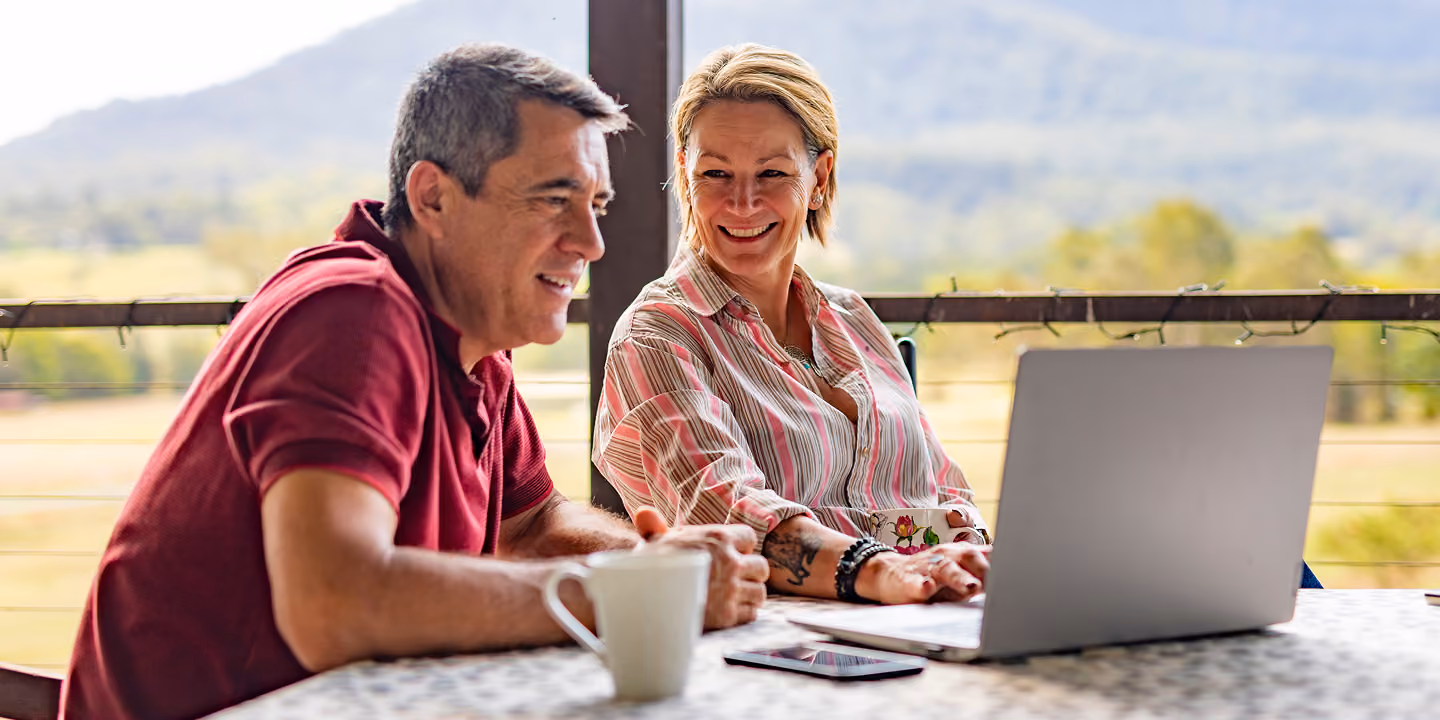 Couple smiling and reviewing their finances together on a laptop outdoors, representing Northeast Wealth's collaborative approach to financial planning