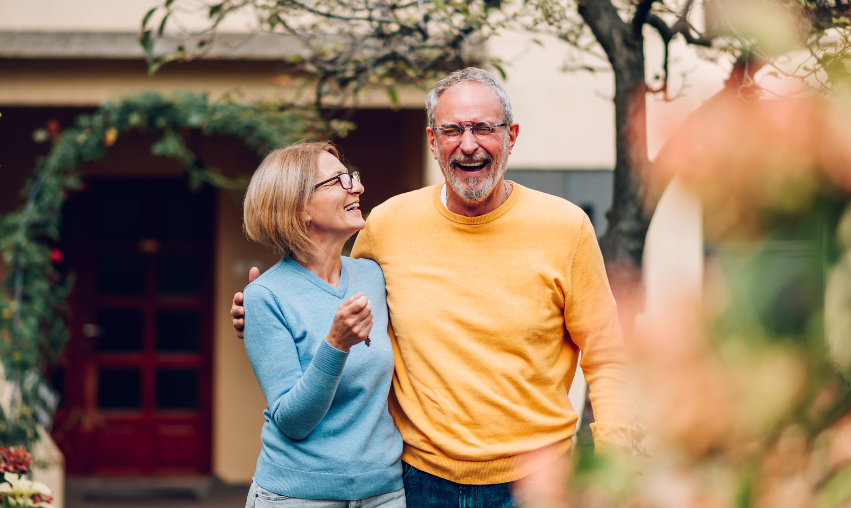 Happy retired couple laughing together outside their home, representing Northeast Wealth's award-winning financial planning that creates direction, clarity, and progress