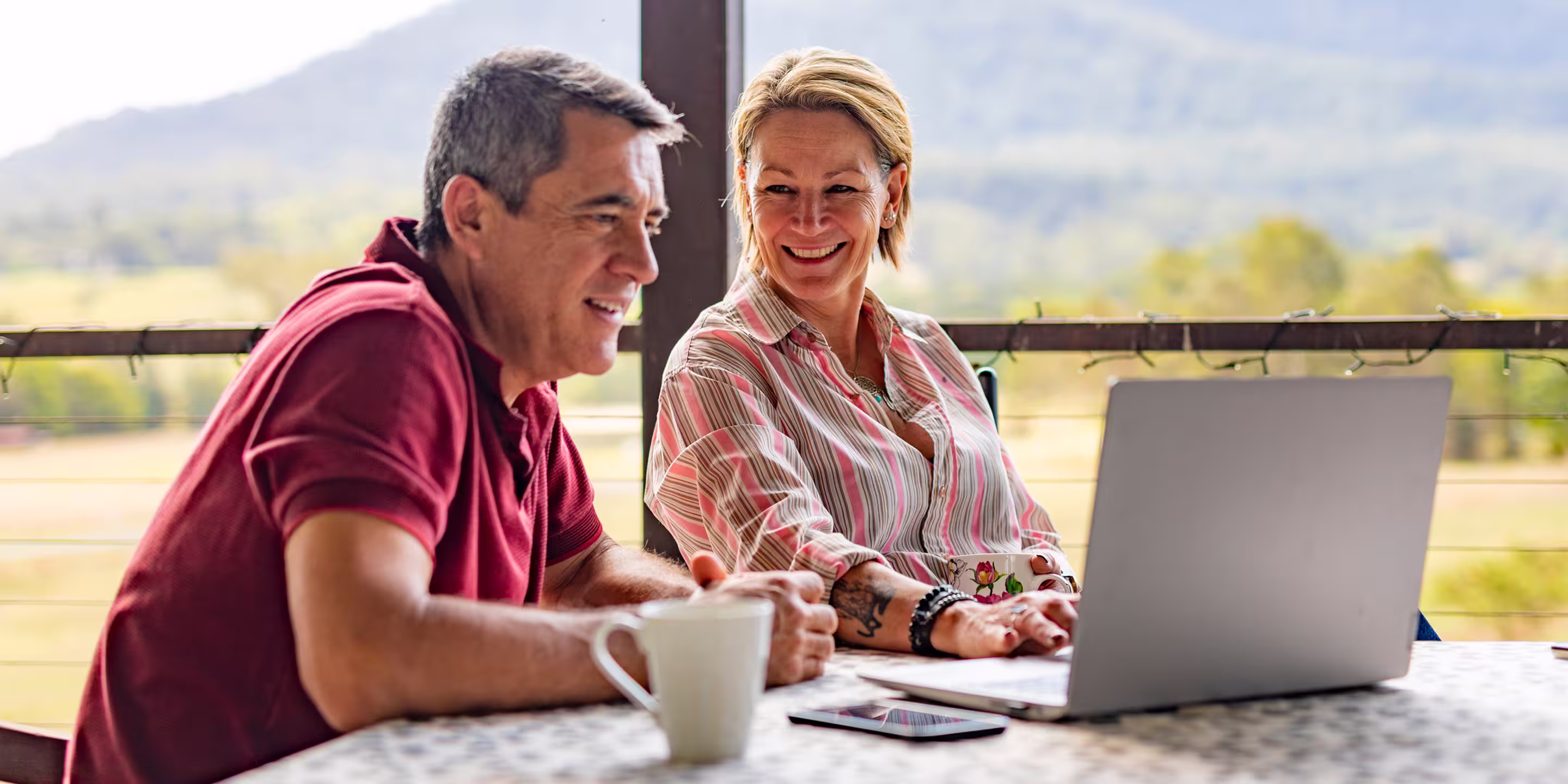 Couple smiling and reviewing their finances together on a laptop outdoors, representing Northeast Wealth's collaborative approach to financial planning