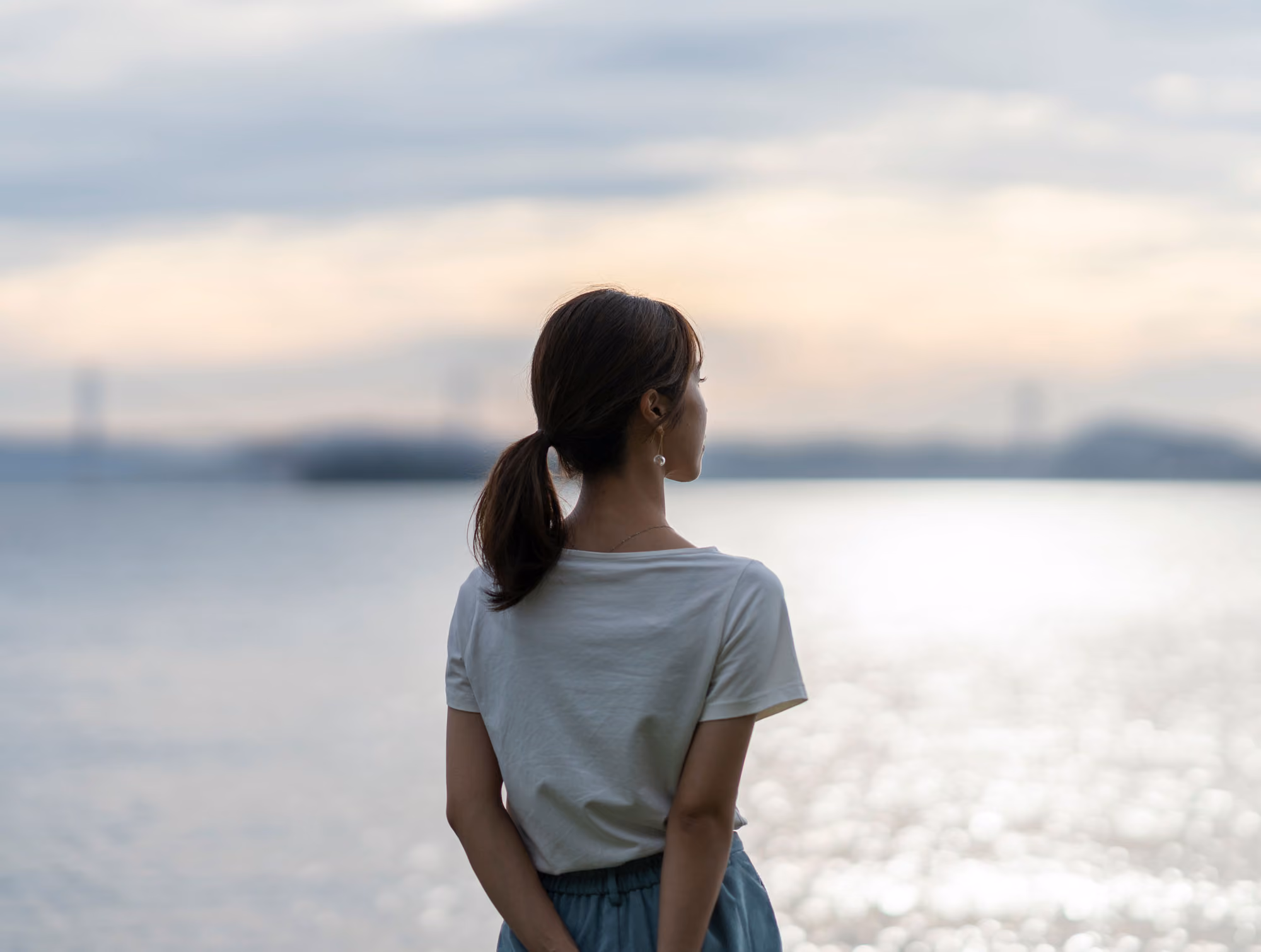 Frau von hinten blickt bei Abendlicht aufs Wasser
