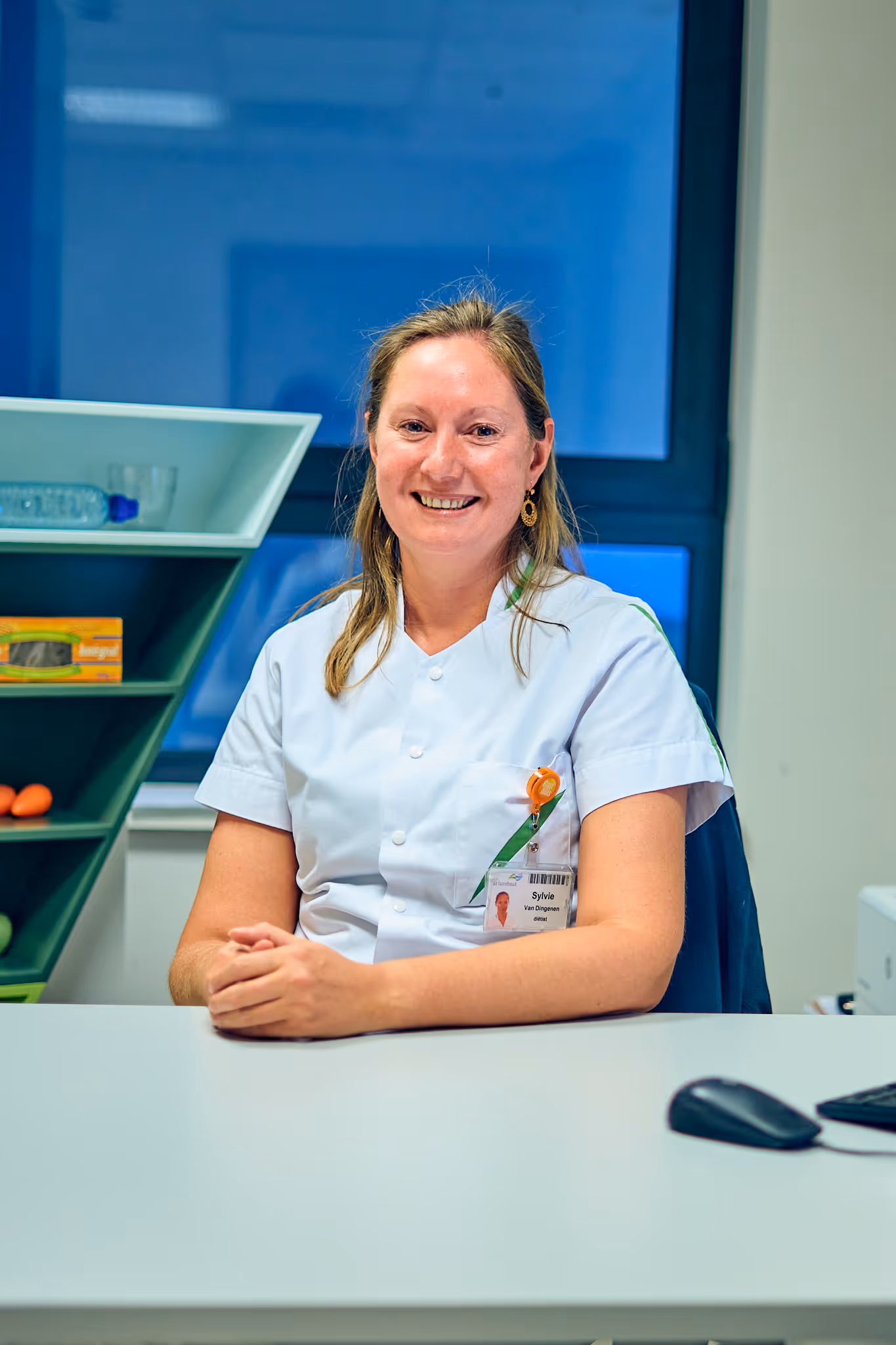 Vrouwelijke zorgverlener glimlacht aan haar bureau in uniform.