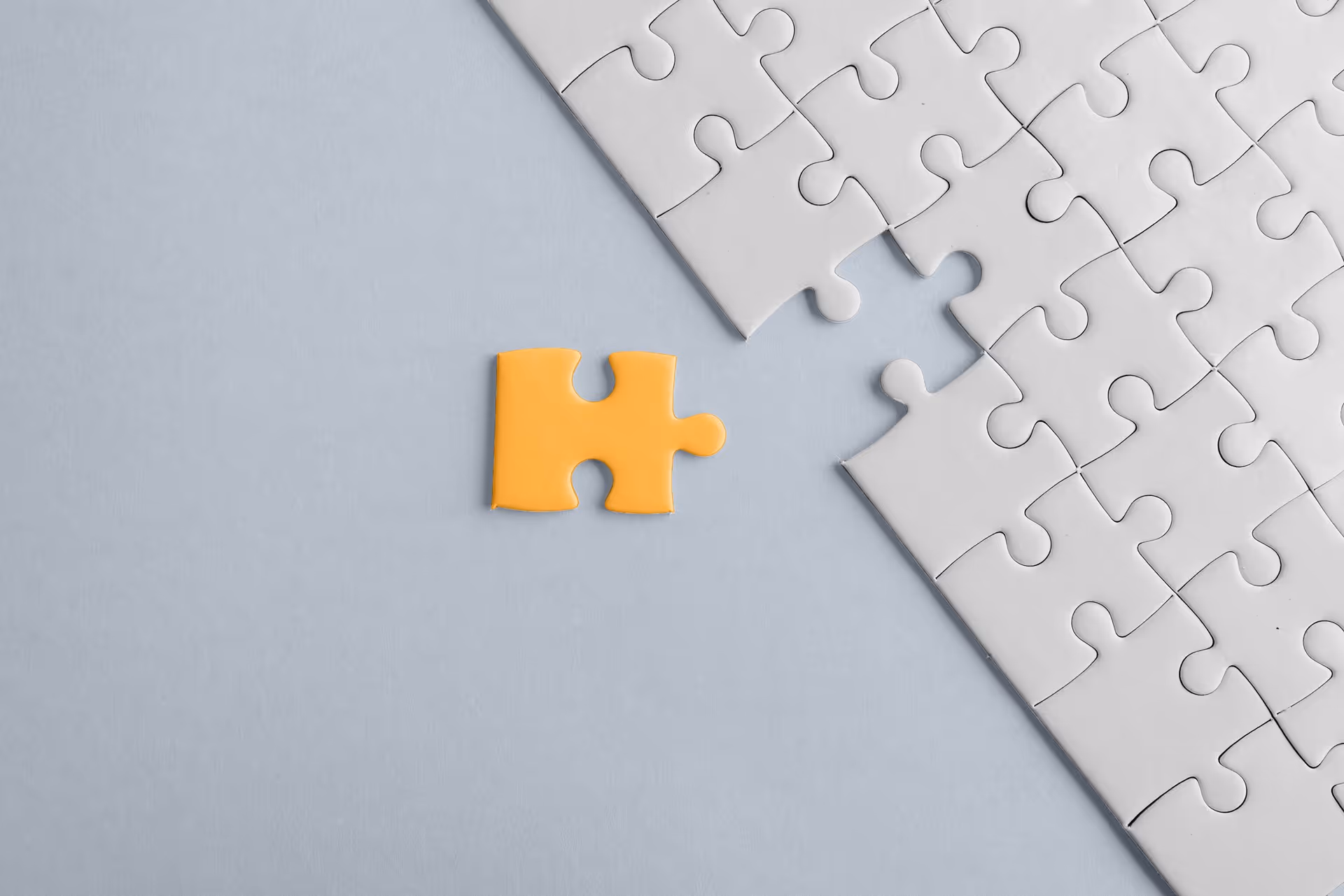 Yellow puzzle piece next to a nearly complete white puzzle with one missing piece on a light gray surface.