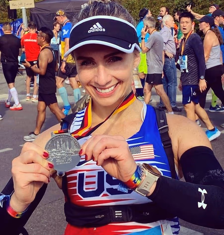 Wild Dog Athletics running client holds up her medal won in a marathon.