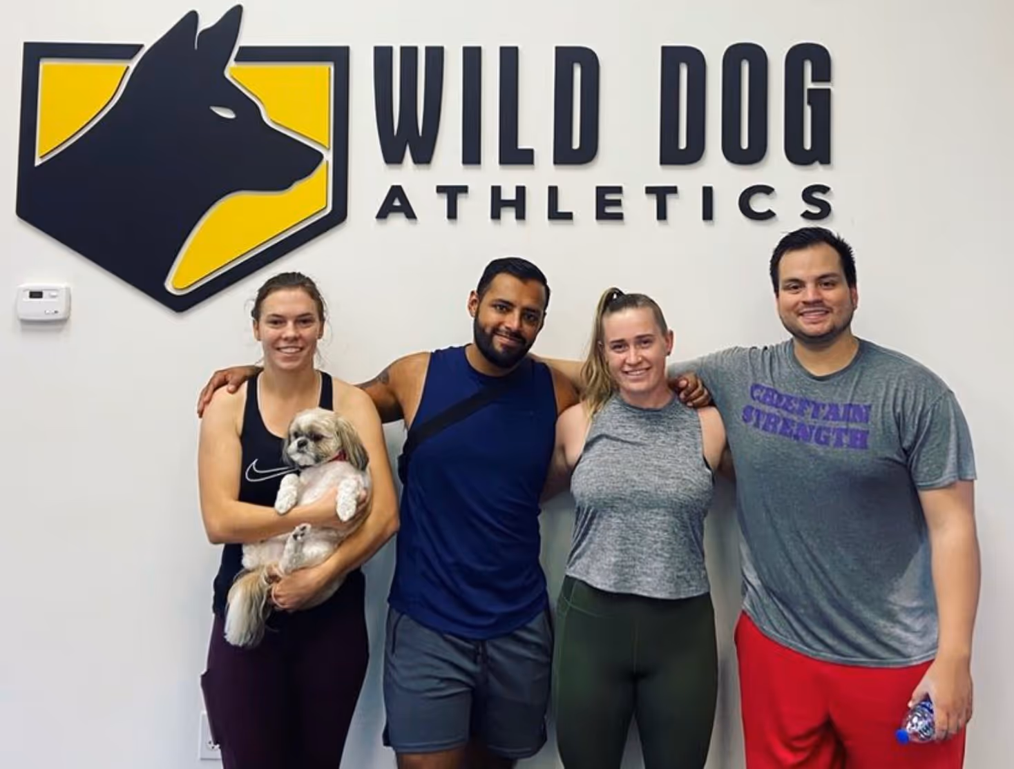 Wild Dog Athletics clients pose for a picture in front of the Wild Dog Athletics sign.