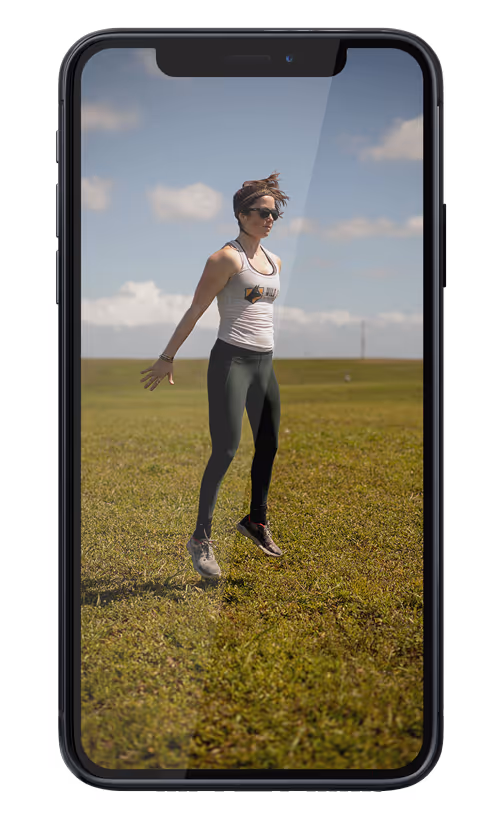 Remote running coach Abby of Wild Dog Athletics performs exercises in a field before trail running as seen on an iphone.